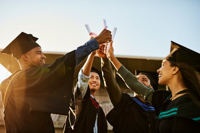 College graduates holding diplomas in the air.