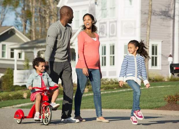Couple walking through suburban neighborhood with youngest child riding a tricycle.