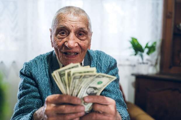 A smiling person seated in a chair who's holding an assorted fan of cash bills. 