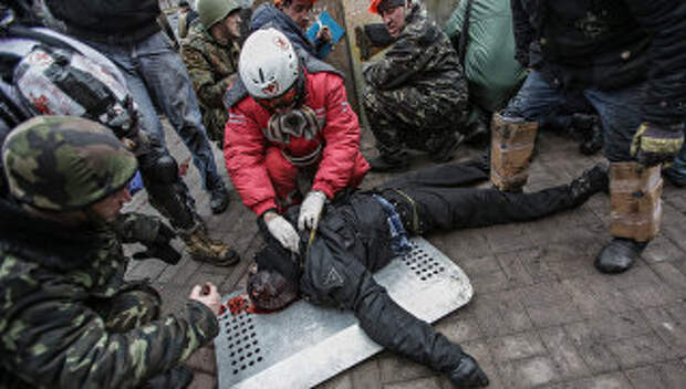 Сторонники оппозиции оказывают помощь раненому во время столкновений на площади Независимости в Киеве
