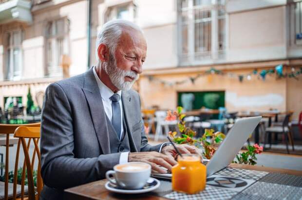 A professionally dressed person using a laptop at an outdoor restaurant.