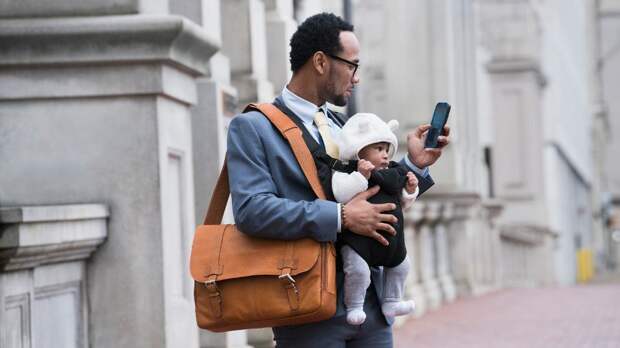 Black businessman with son in baby carrier texting on cell phone