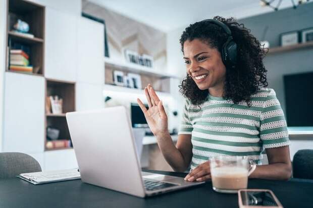 A woman works from home as she smiles and waves to a video call on her laptop.