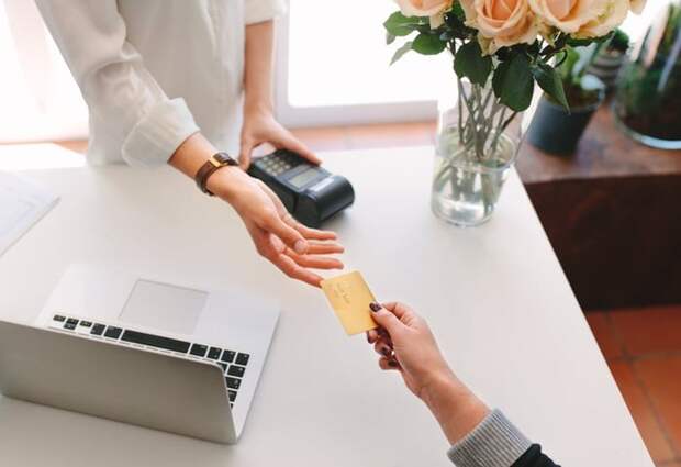 A woman handing her credit card to a store employee for payment.