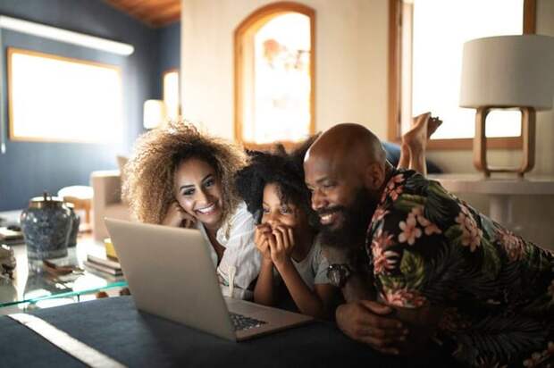 A smiling mom and dad with their child in the middle all watching a movie on a laptop.
