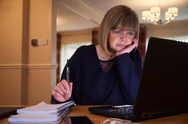 A middle-aged adult sorts their home finances with a laptop and notebook.