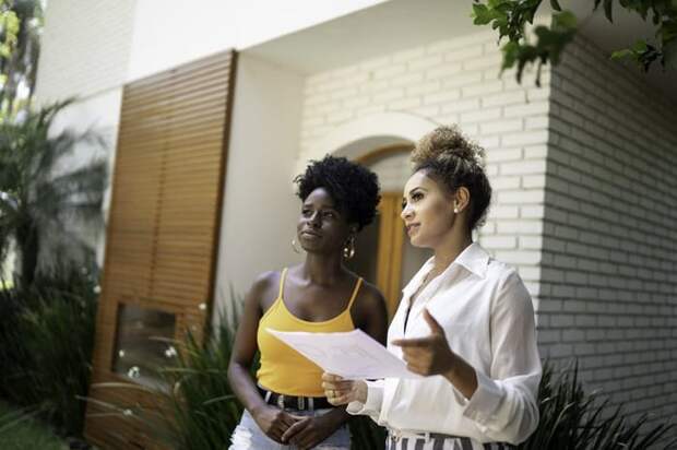 A woman chats with her realtor while standing outside a nice house.