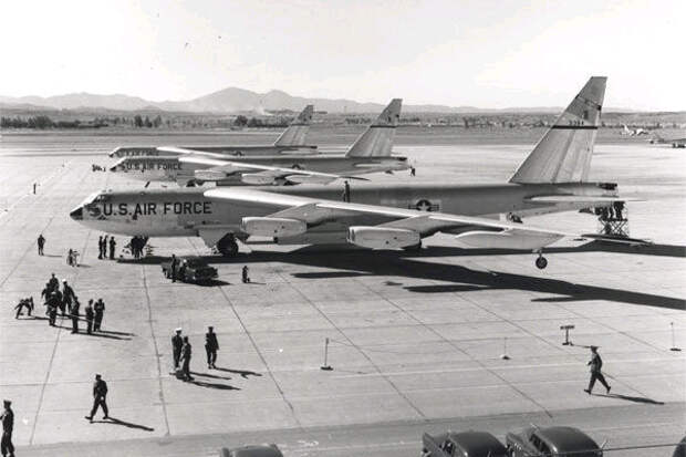 Black-and-white photo of three B-52s parked close together facing left, as personnel on the ground prepare them for departure