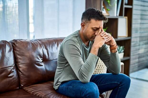 A person sitting on a couch with eyes closed and hands on forehead.
