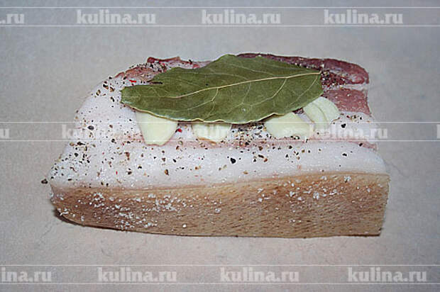 Выкладываем кусок сала. Поверх также кладем лаврушку и чеснок.