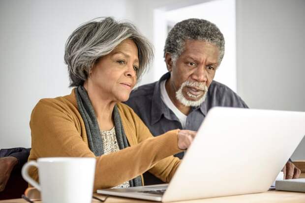 A couple seated at a table and sharing a laptop while intently viewing content.