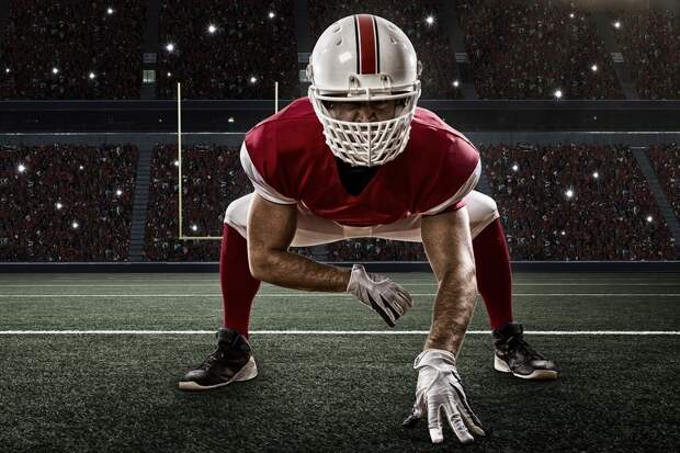 Football Player with a red uniform on the scrimmage line on a Stadium.