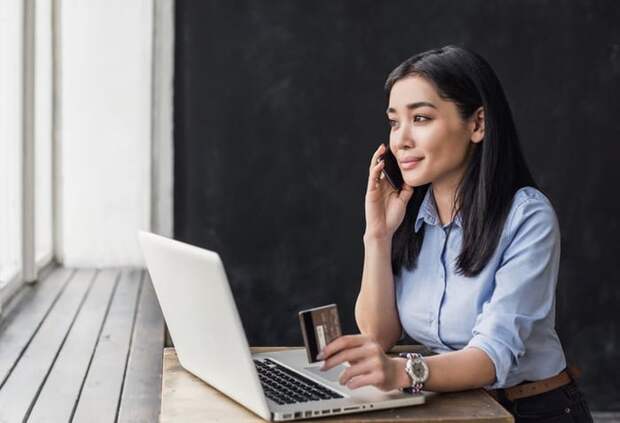 A woman holding a credit card and making a phone call.