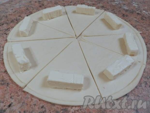 На край каждого сектора положить по 1/3 кусочка сыра Kiri, затем завернуть каждый сектор из дрожжевого слоеного теста в рогалик от края к центру.