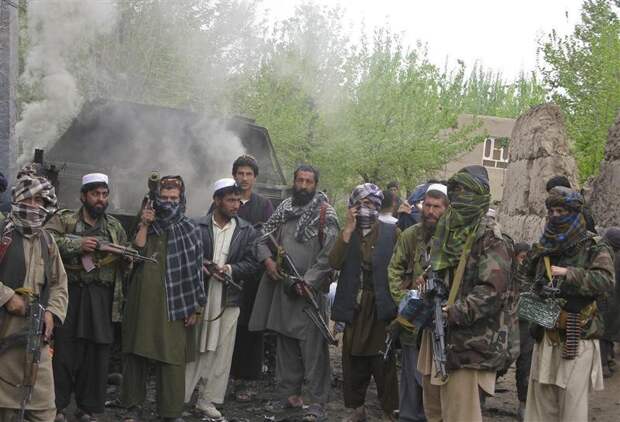 Taliban insurgents pose in front of a burning German military vehicle in Isaa Khail village of Char Dara district of the northern Kunduz Province