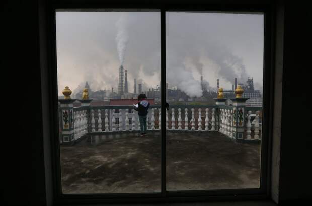 Дым, вздымающийся из металлургического завода, и девочка, которая читает книгу на балконе в Цюйчжоу загрезнение, китай, природа