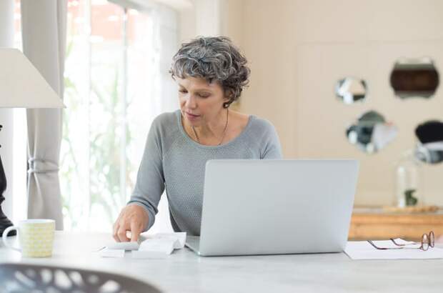 A person looking at a document while sitting in front of a laptop.