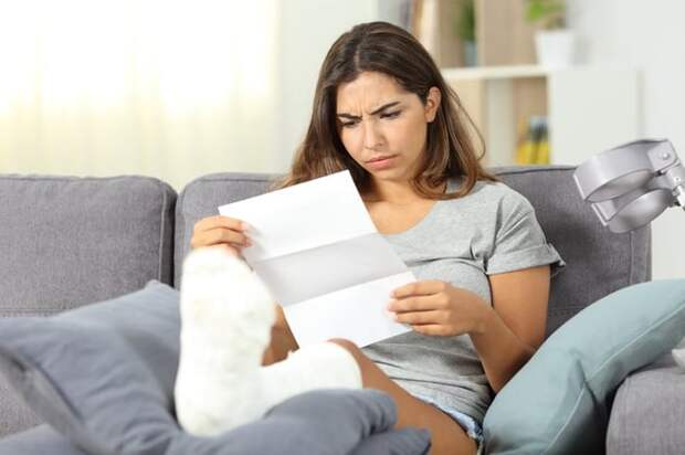 A woman with a cast on her leg looks at a medical bill