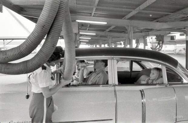 Холодный воздух подается в машину, пока ее пассажиры наслаждаются едой в ресторане формата drive-in. Хьюстон, 1957 год история, ретро, фотографии