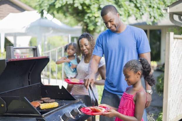 Family grilling hamburgers, hotdogs, and corn in back yard.