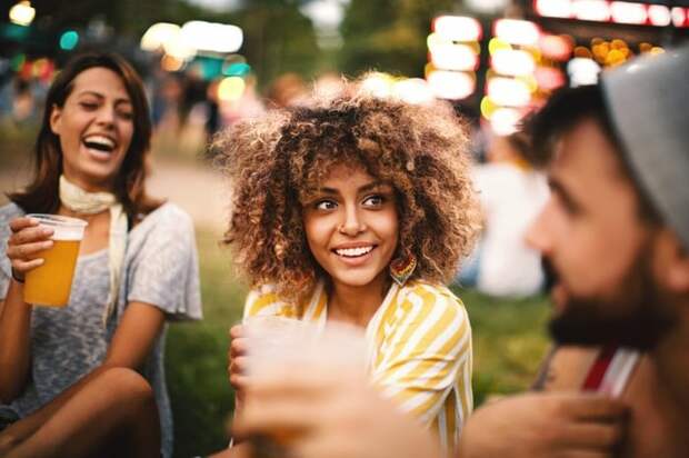 Three friends laughing and drinking beer at an outdoor summer concert.