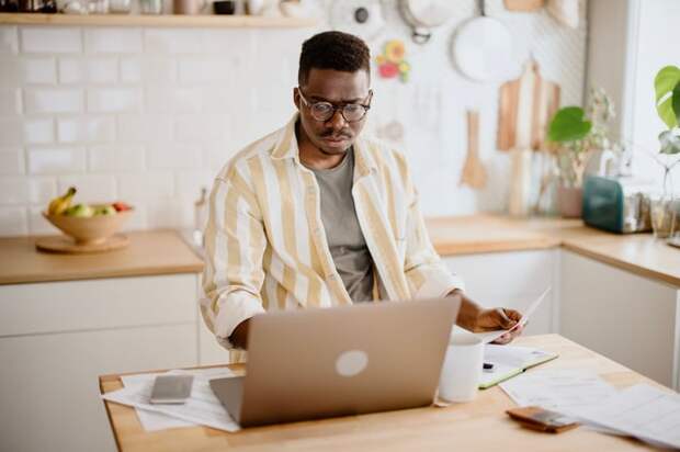 Person standing at a kitchen island looking down at a laptop.