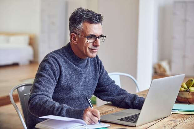 A person at a laptop holding a pen.