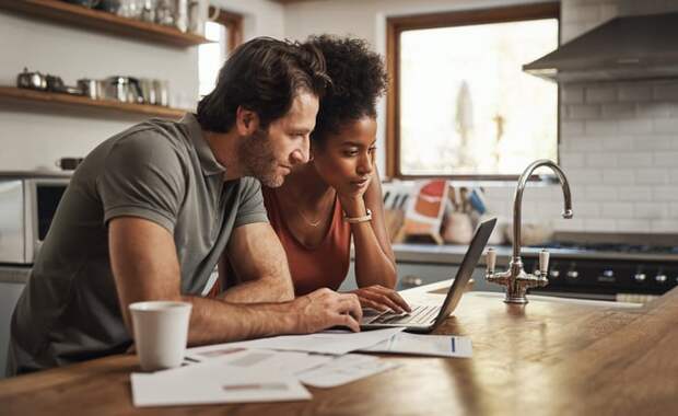 Couple researching on computer in a home kitchen.
