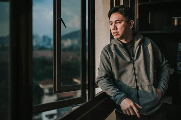 A worried person looking out the window of their apartment.