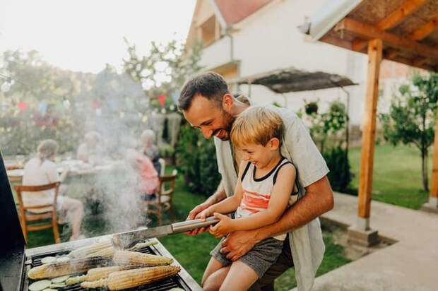 Father and son grill corn during a cookout on the patio.