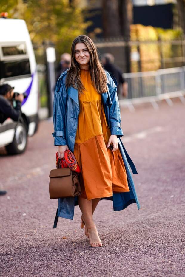 Девушка в оранжевом платье свободного кроя, синий плащ и коричневая сумка