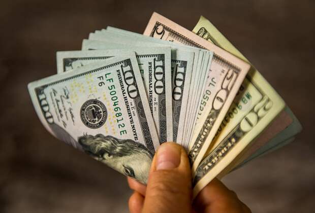 A hand holding a fanned and folded stack of money.