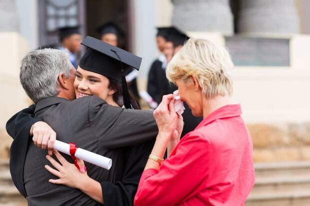 Female college grad hugging her dad next to her tearful mom.