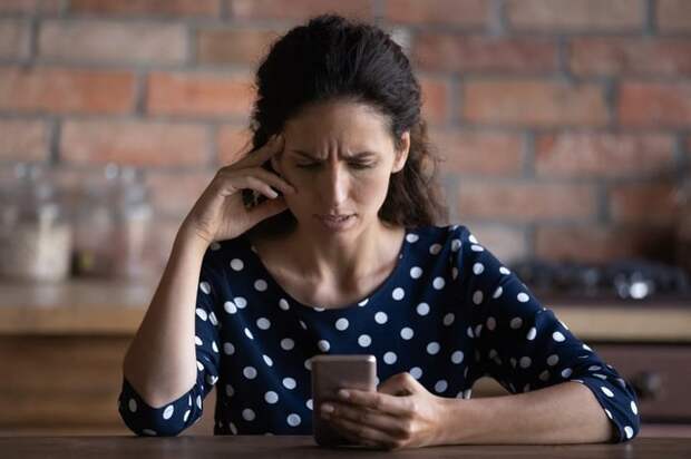 An upset person with a creased brow looks at their smartphone screen.
