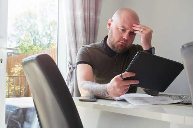 A homeowner looks worried as he reads through his household bills at the dining table.