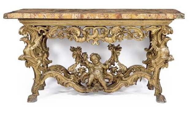 AN ITALIAN CARVED GILTWOOD SIDE TABLE MID-18TH CENTURY With a siena marble top, above a pierced scrolled frieze centred by a pair of winged dragons, the sides with foliate and S-scrolls, the scrolled supports carved with birds with out-stretched wings and joined by stretchers centred by a seated putto within a bower and flanked by surface dragons and with hairy hoof feet, Christie's.