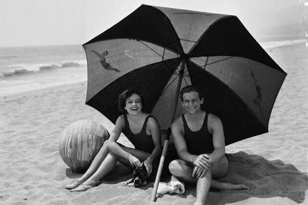 Молодожены Джоан Кроуфорд и Дуглас Фэрбенкс отдыхают со своей собакой в тени пляжного зонтика на пляже Каталина, 1929. Фото Джорджа Рейнхарта. звезды, знаменитости, лето, пляж, прошлое, ретро, фотография