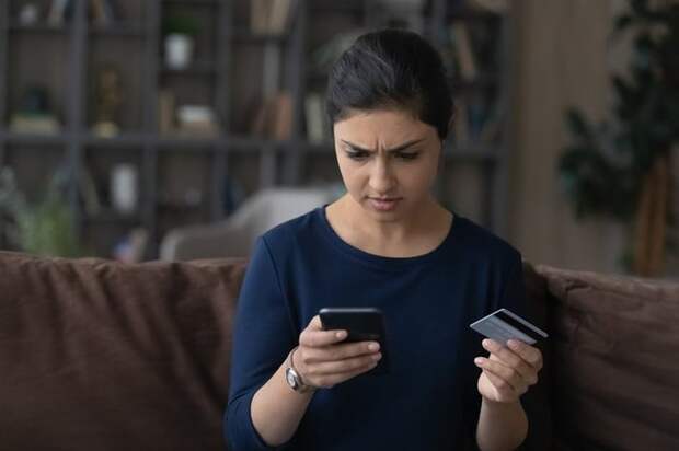 Someone frowns at their smartphone while holding up their credit card.