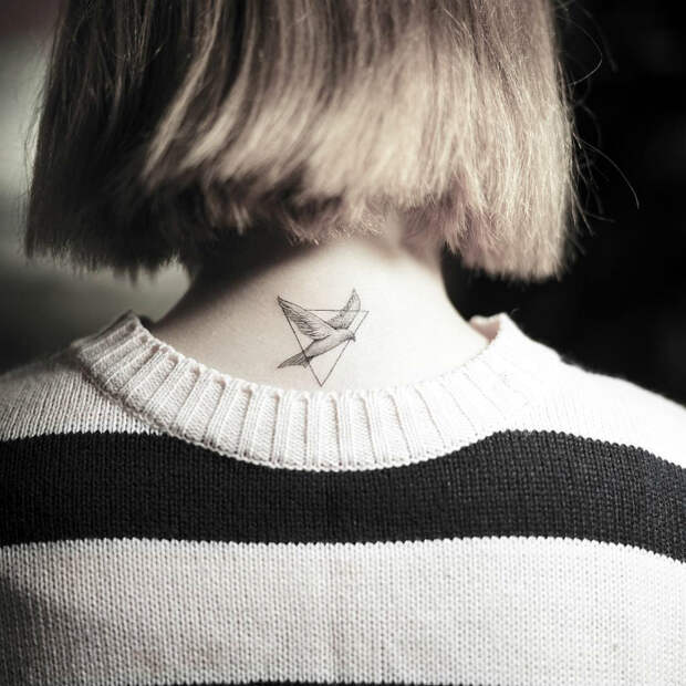 Минималистичное тату с изображением птицы в треугольнике на девичьем затылке.