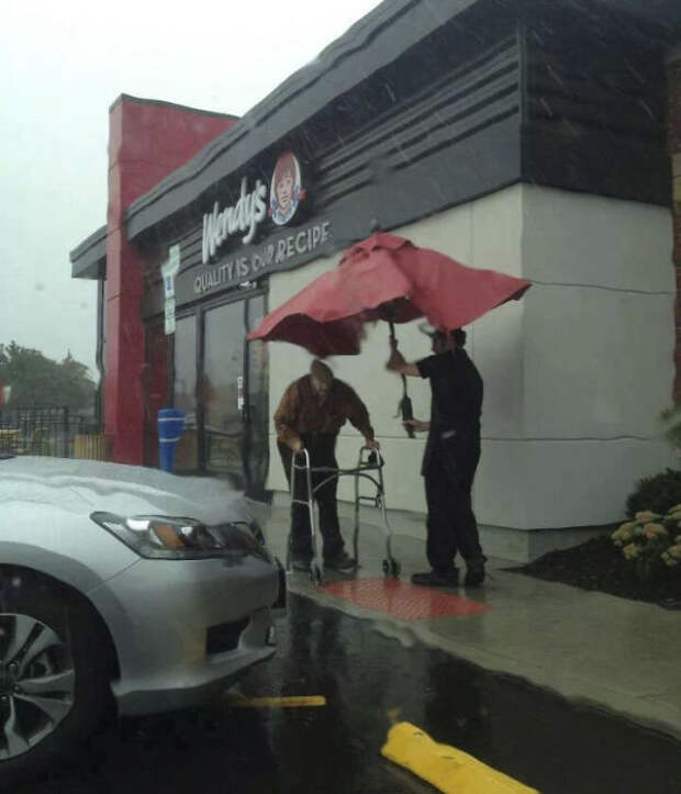 Сотрудники магазина вынесли зонтик со стола на улицу, чтобы помочь пожилому мужчине пройти под дождем к машине.