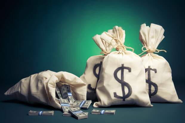 Four canvas money bags with dollar signs on them, and one spilled open, revealing bundles of bills.