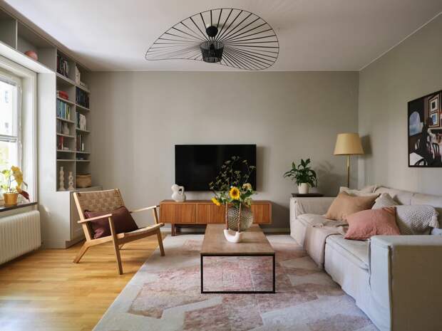 На полу в гостиной — дубовый паркет. Для стен выбран приятный светло-оливковый оттенок (хотя я не имею ничего против белых стен). Ковер гармонично сочетается с текстилем на диване. А картина на стене — с лампой. Но больше всего мне понравилось, как здесь оформлена библиотека. Хорошее решение, которое экономит место