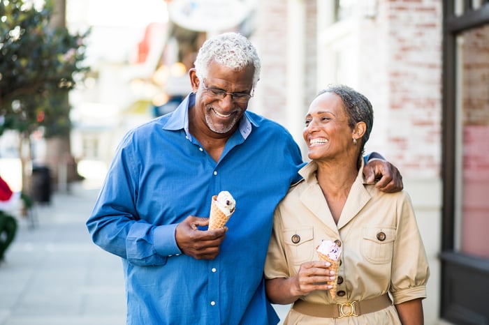Two smiling people eating ice cream and walking down the street.