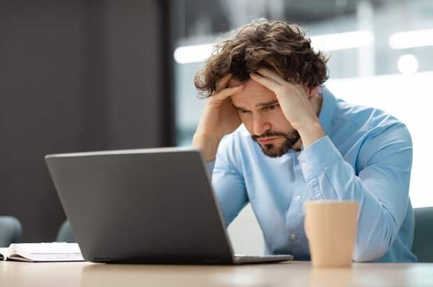 A person at a laptop holding his head.