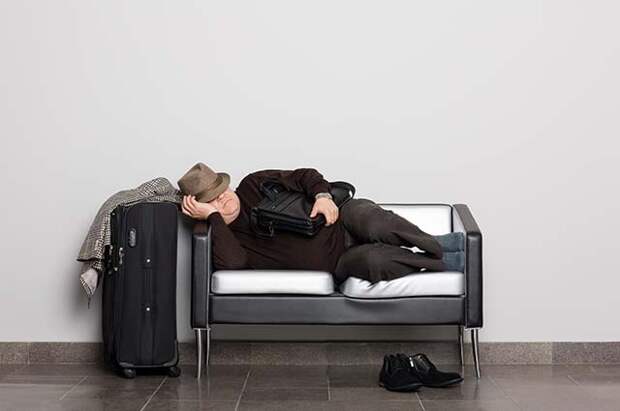 Мужчина спит на диване, рядом стоит чемодан